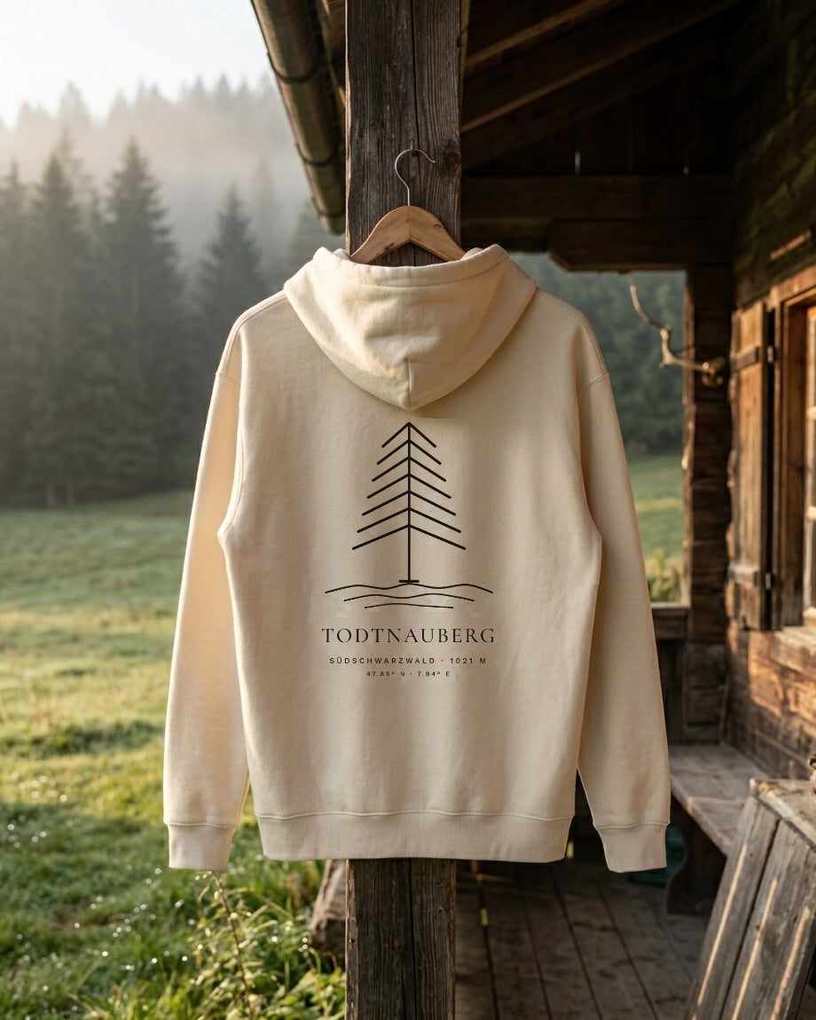 Rückseite Hoodie Höhenlage in Natural Raw mit Tannen-Motiv und Schriftzug Todtnauberg, an einer Almhütte vor nebligem Tannenwald